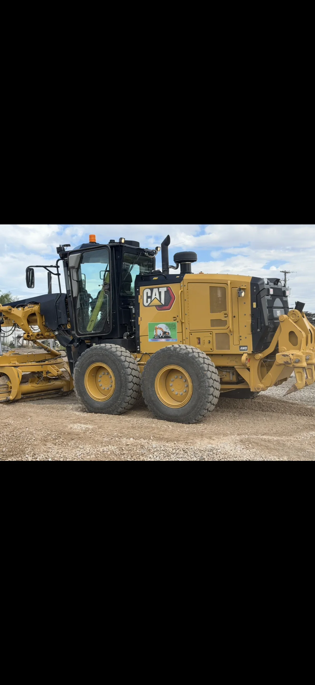 Yellow Caterpillar motor grader with enclosed cab and AWD badge on gravel and dirt grading site