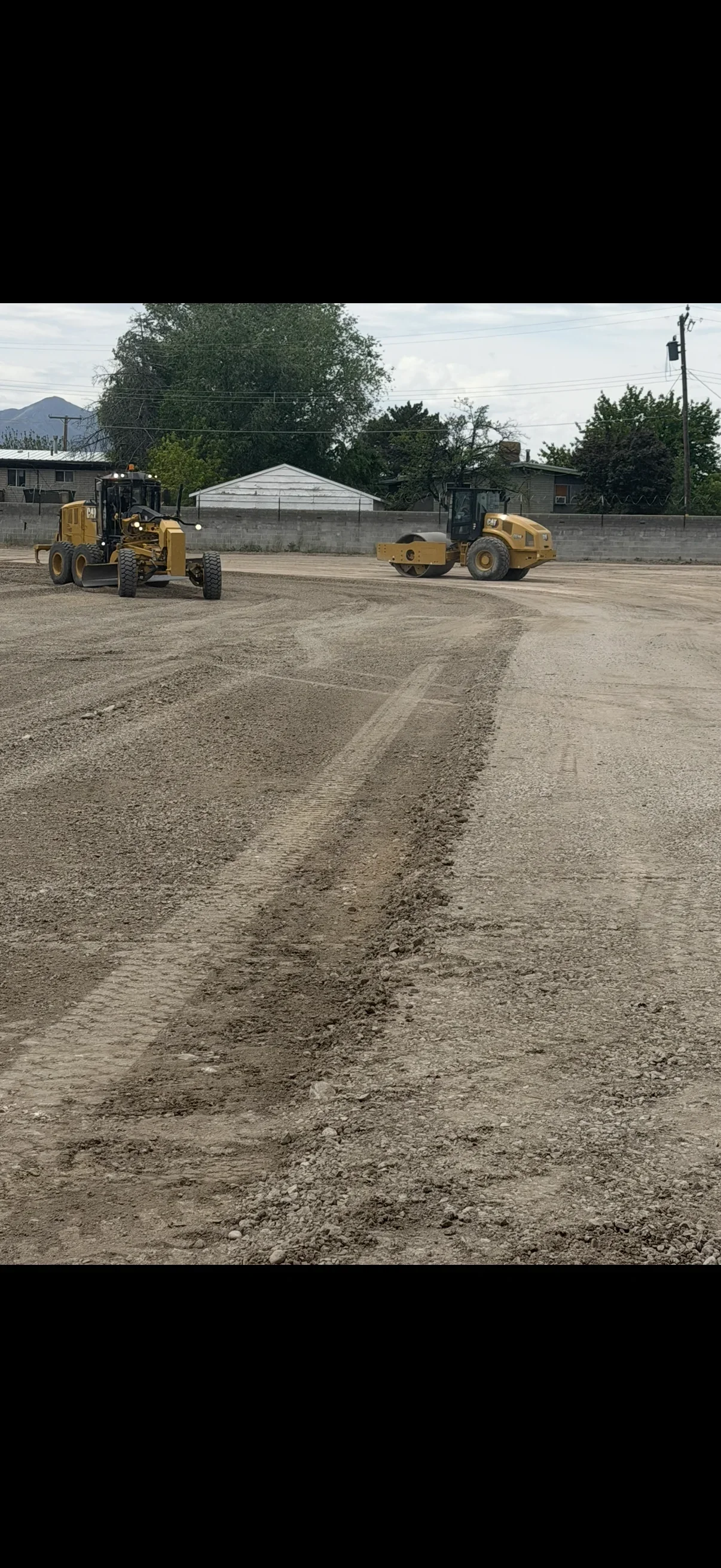 Caterpillar motor grader and smooth drum roller grading and compacting gravel on a lot